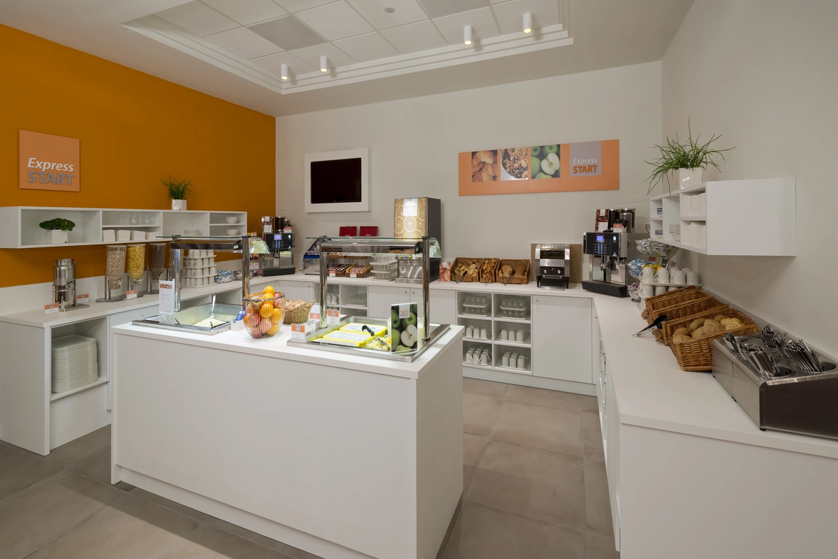 Verschiedene Lebensmittel sind als Buffet auf Tischen platziert. Unter Anderem sieht man Kaffee, Brötchen und Obst