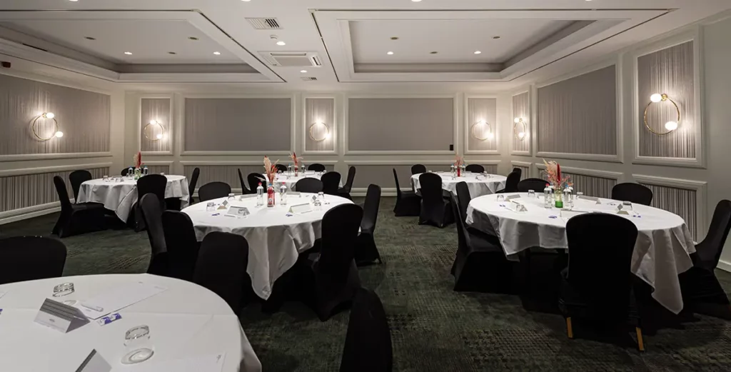 Der Ground Floor Meetingraum mit runden Tischen, an dene jeweils 5 dunkele Stühle stehen.